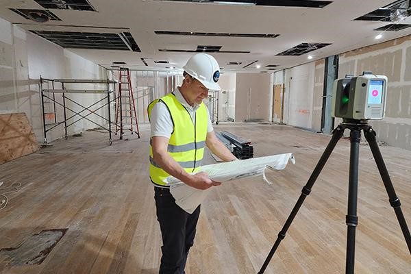 3D laser scanning technician reviewing drawings with Leica LiDAR scanner capturing existing building conditions on site