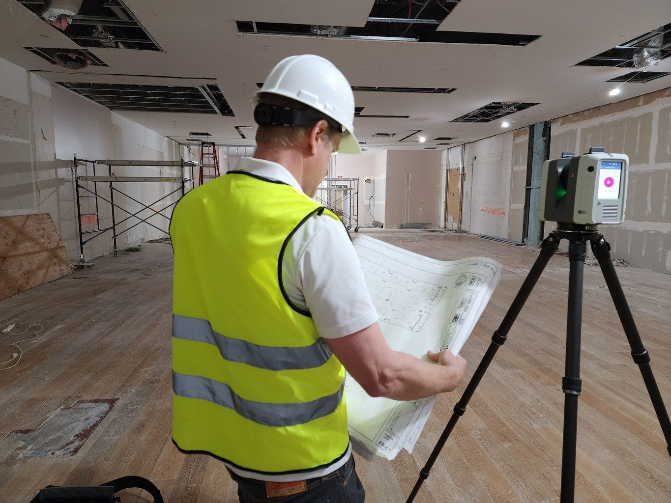 Scan technician reviewing plans while performing 3D laser scanning in a room for as-built documentation.